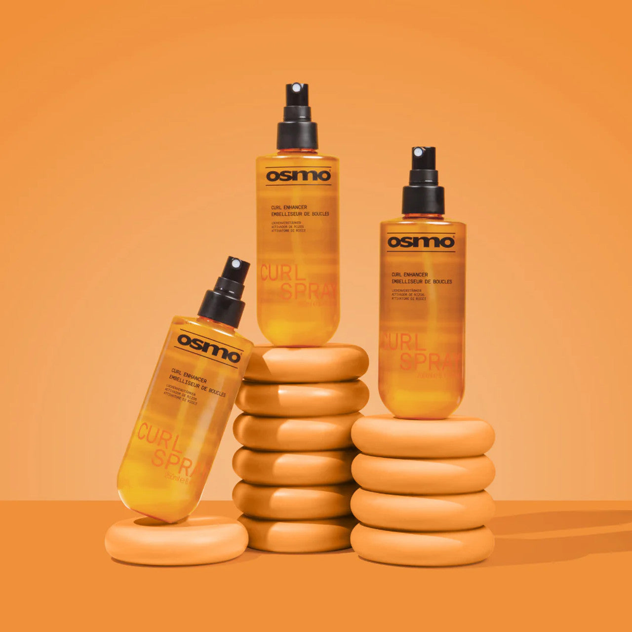 Three bottles of Osmo Curl Spray on an orange background