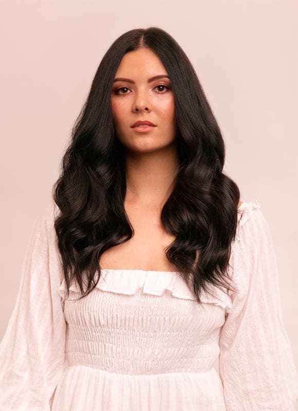 Woman with long, wavy hair wearing a light pink dress against a beige background