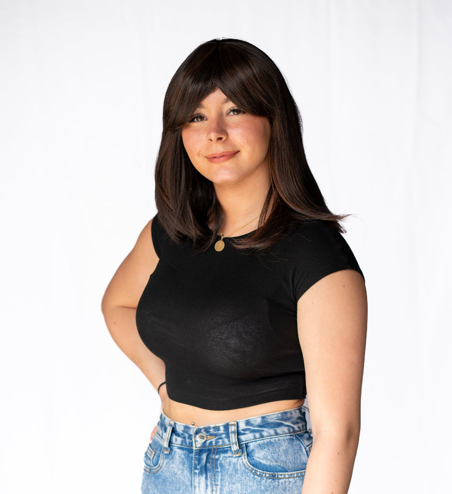A woman wearing a dark brown synthetic wig with a sweeping side fringe, paired with a black top and blue jeans.