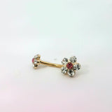 Gold belly button ring with floral design and red gemstones on a white background