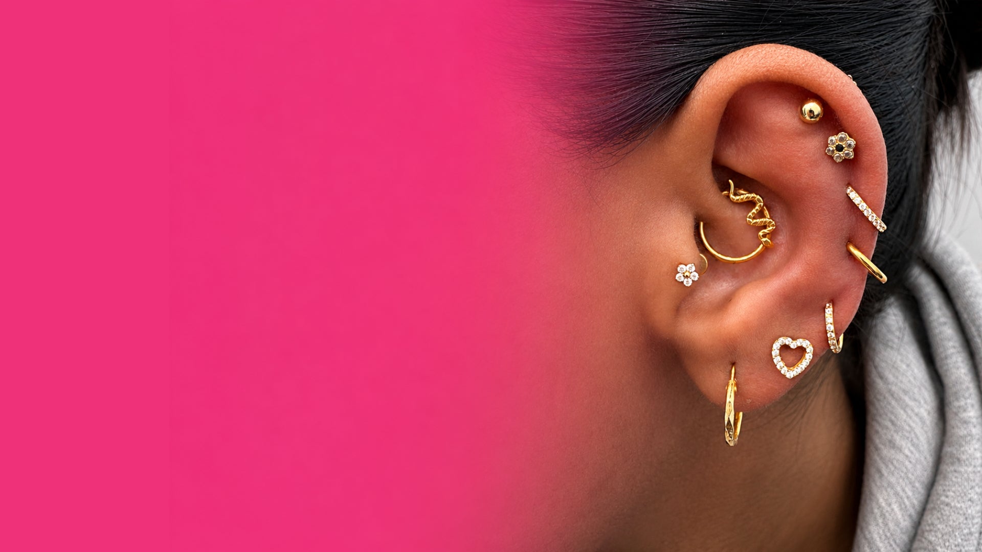 Close-up of an ear with multiple gold earrings against a pink background