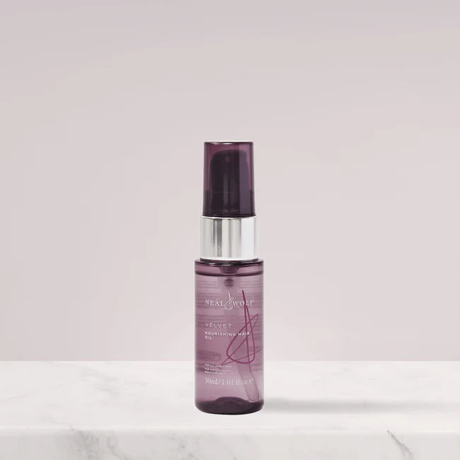 Purple spray bottle of Neal and Wolf Hair Oil on a light pink background
