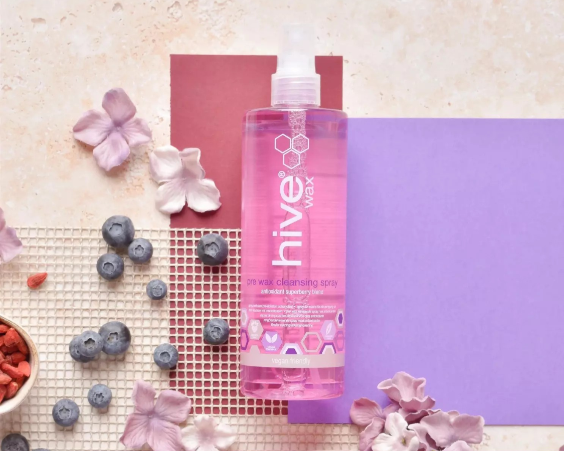 Bottle of 'hive wax' pre cleansing spray on a textured surface with flowers and berries