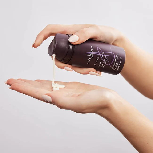 a pump bottle of neal and wolfe pliable paste being squeezed out onto an open palm