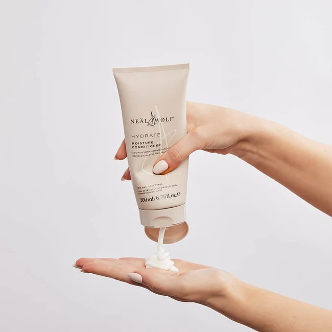 Neal and wolf conditioner bottle in beige, being squeezed out onto an open palm