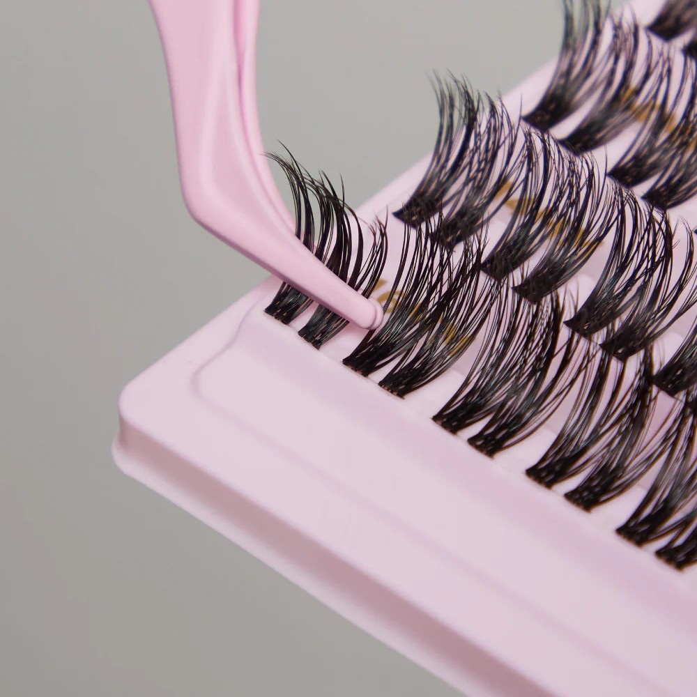 close up of tatti lash eyelash clusters displayed in a pink box, with pink tweezers holding a pair